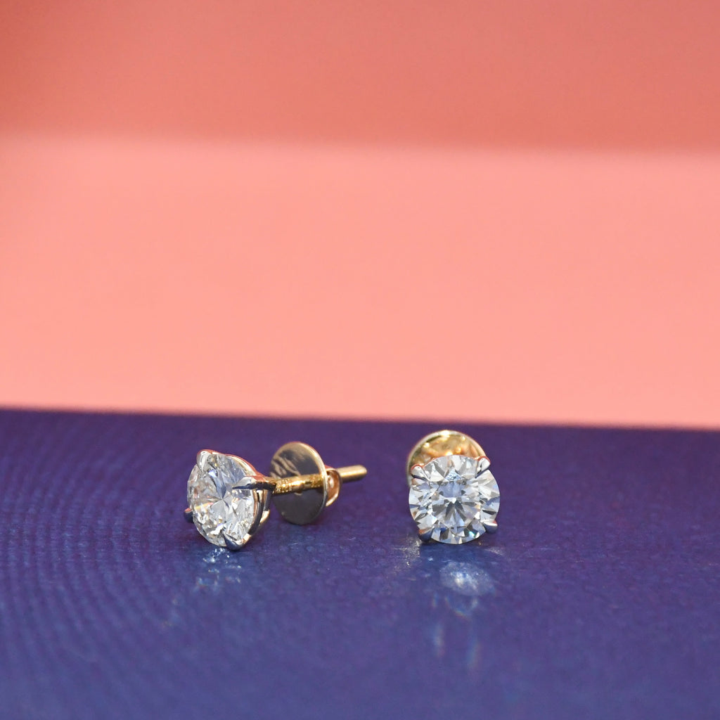 Gold stud earrings with clear diamonds on a blue and pink gradient background