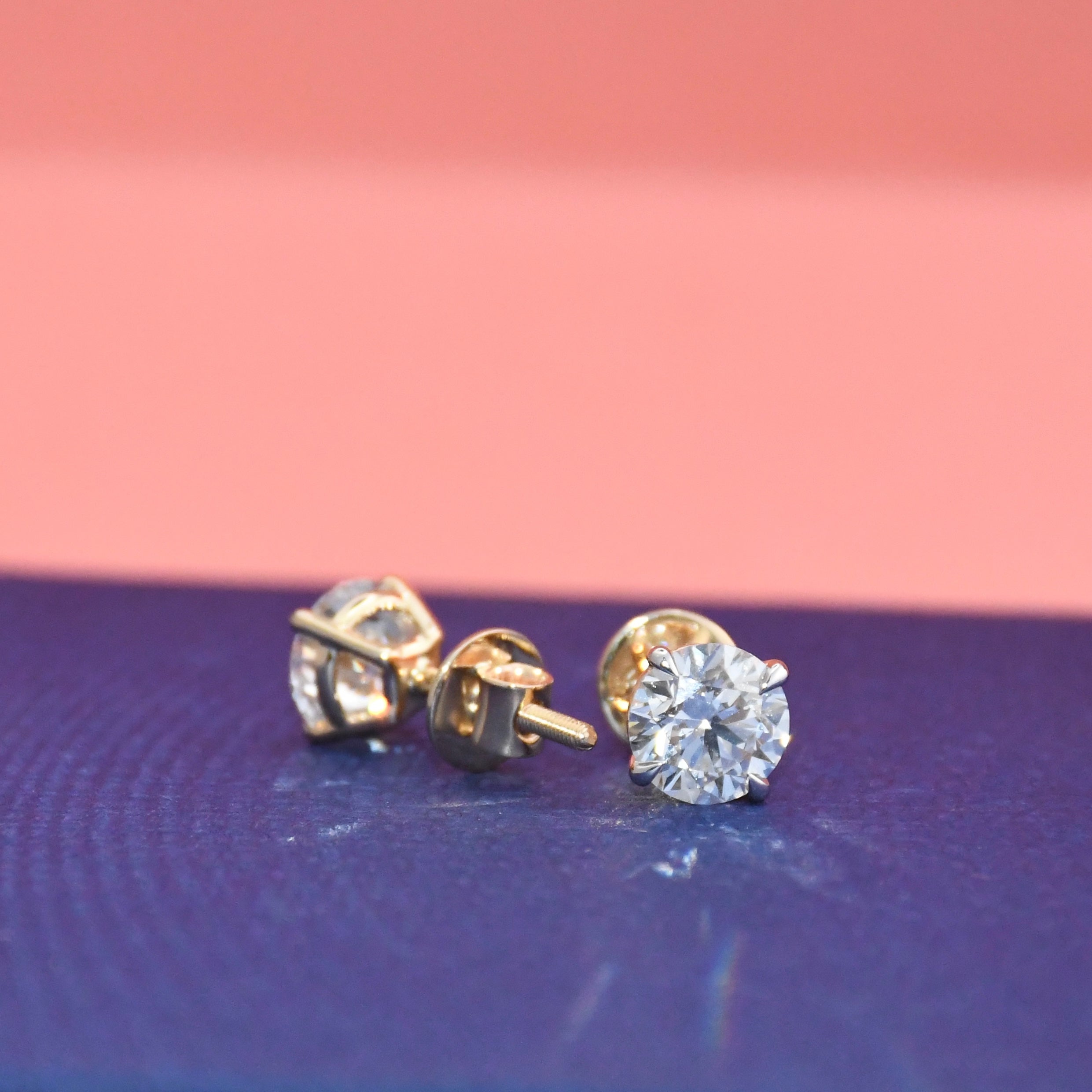 Gold diamond stud earrings on a blue and pink gradient background