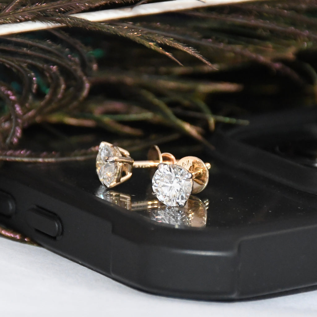 Diamond stud earrings on a black phone case with peacock feathers in the background