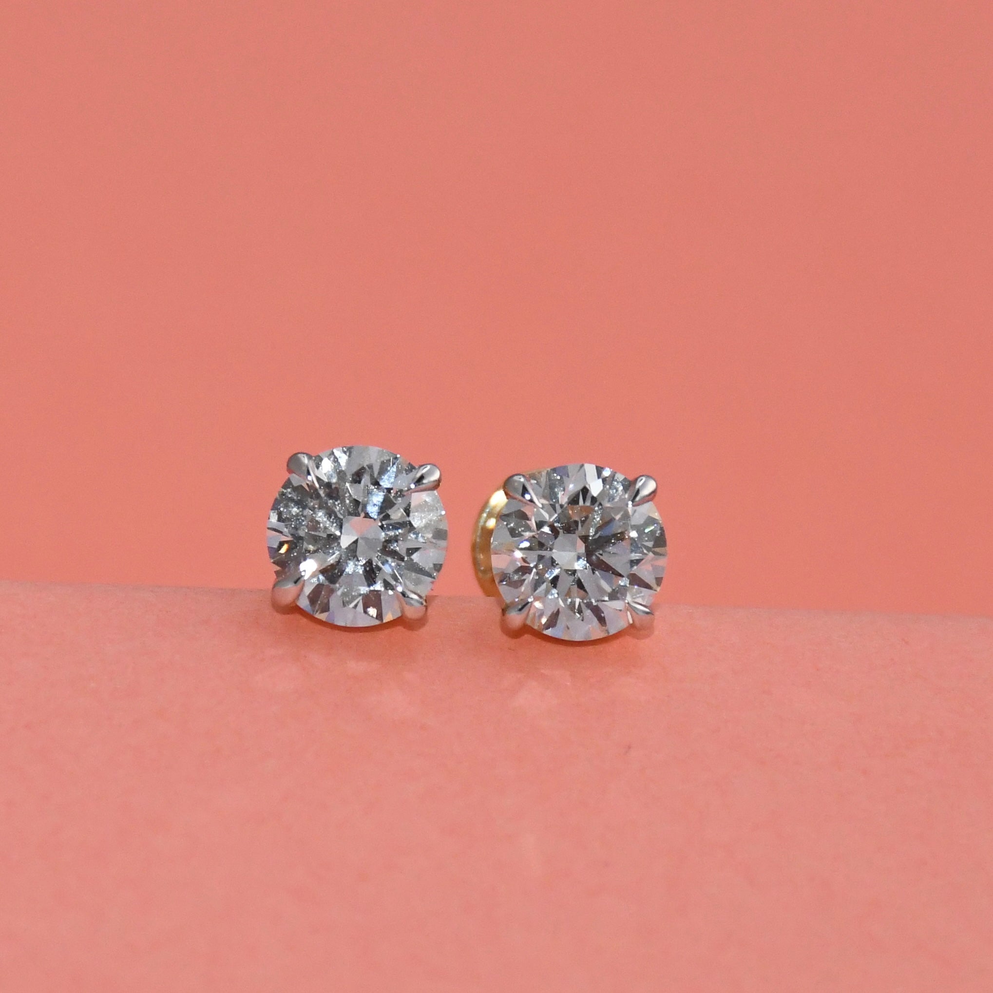 Pair of diamond stud earrings on a peach background