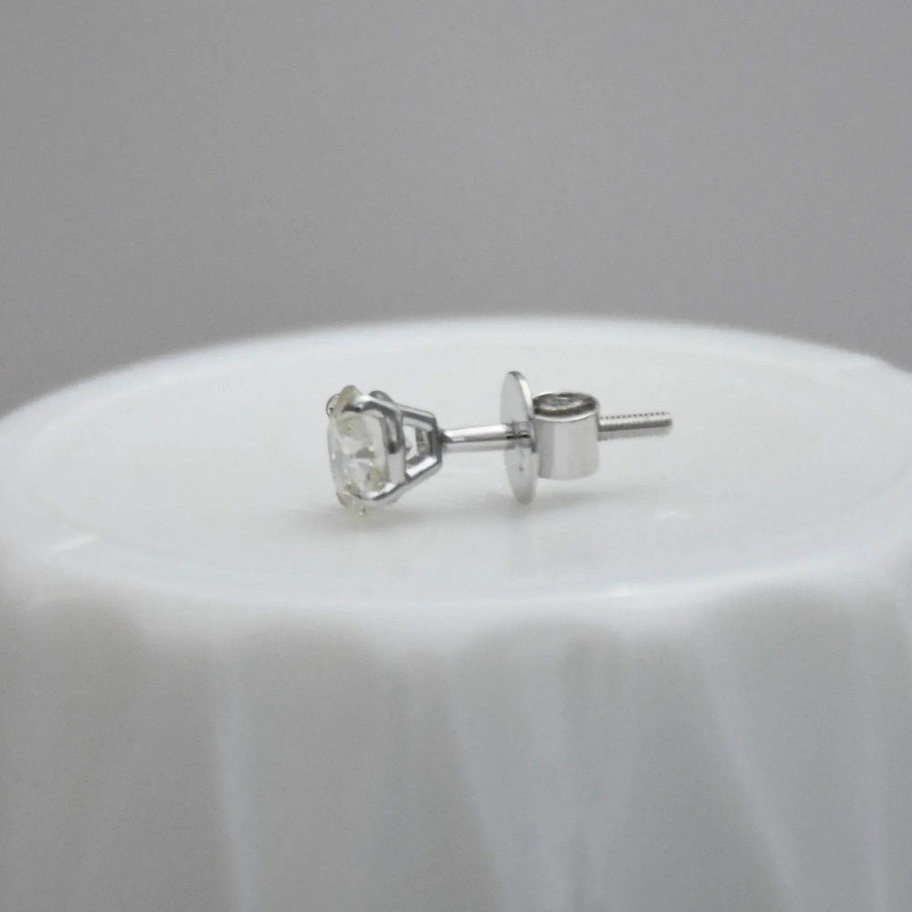 white gold stud earring on a white surface with a gray background