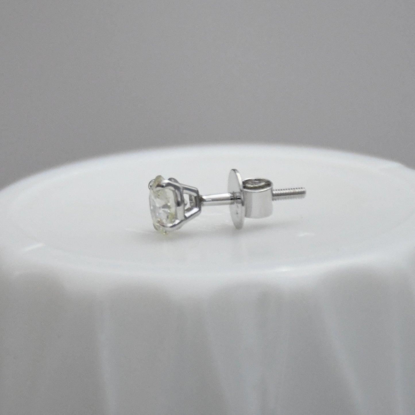 white gold stud earring on a white surface with a gray background
