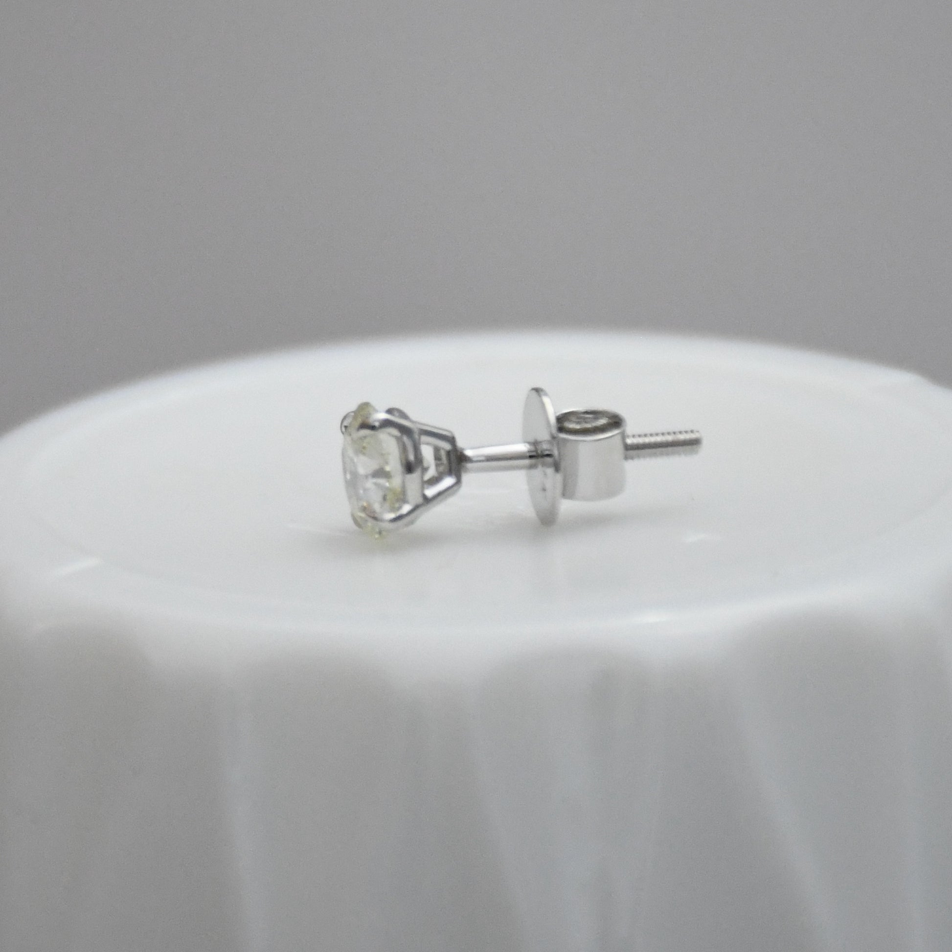 white gold stud earring on a white surface with a gray background