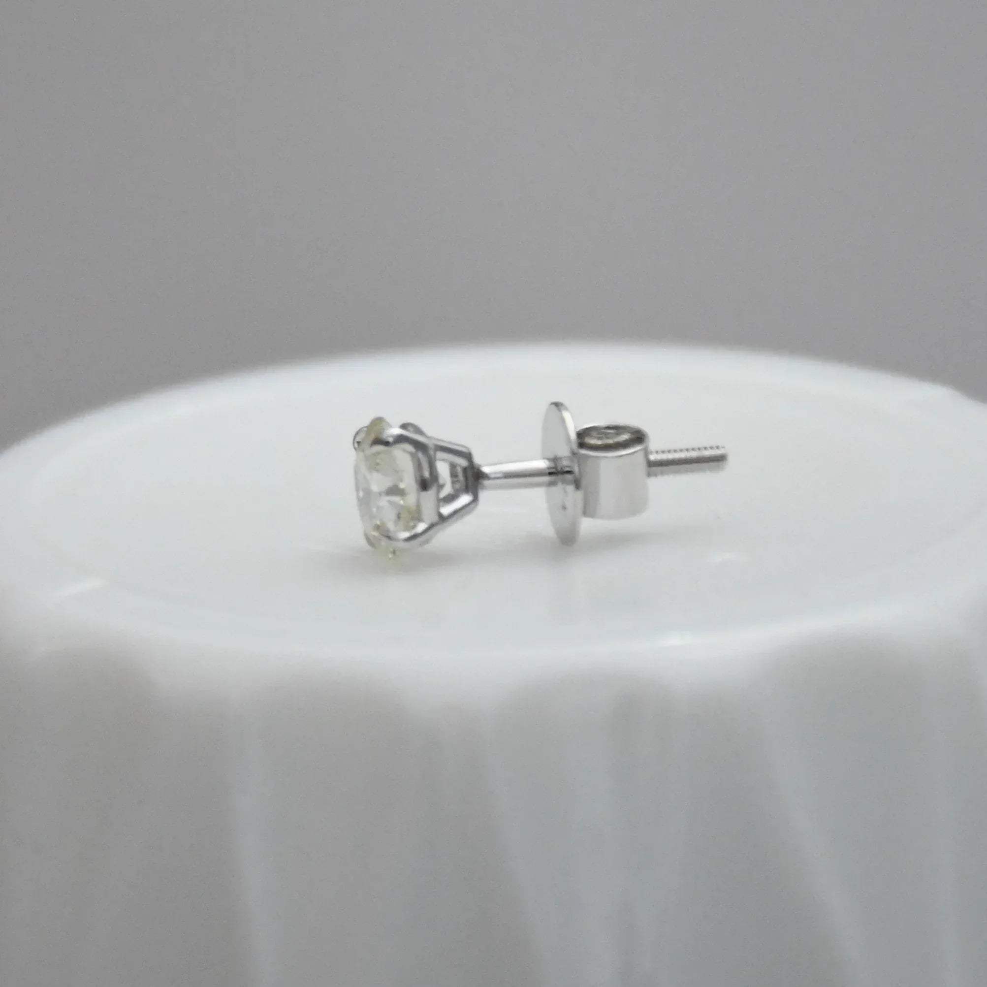 white gold stud earring on a white surface with a gray background