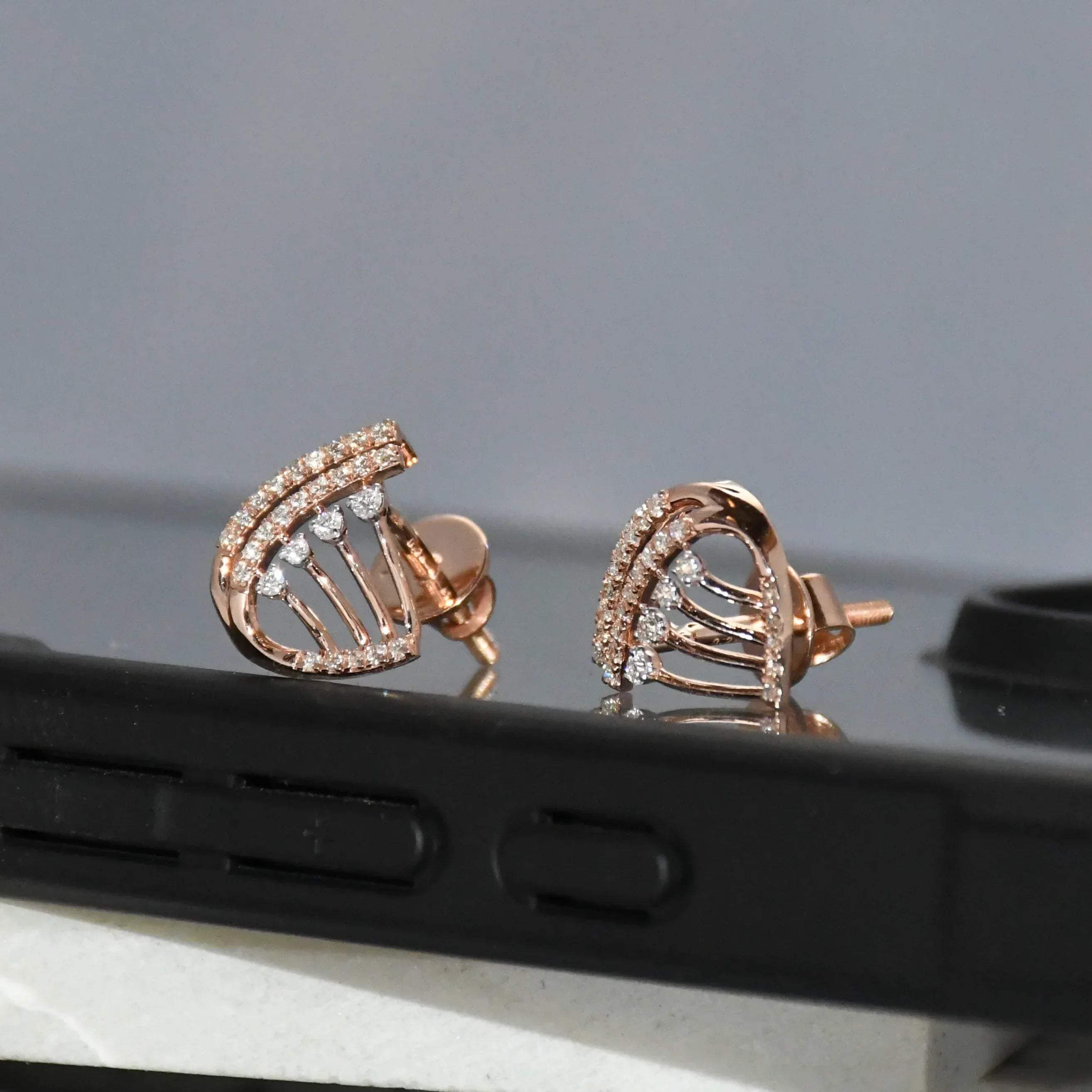 Rose gold earrings with diamonds on a reflective surface