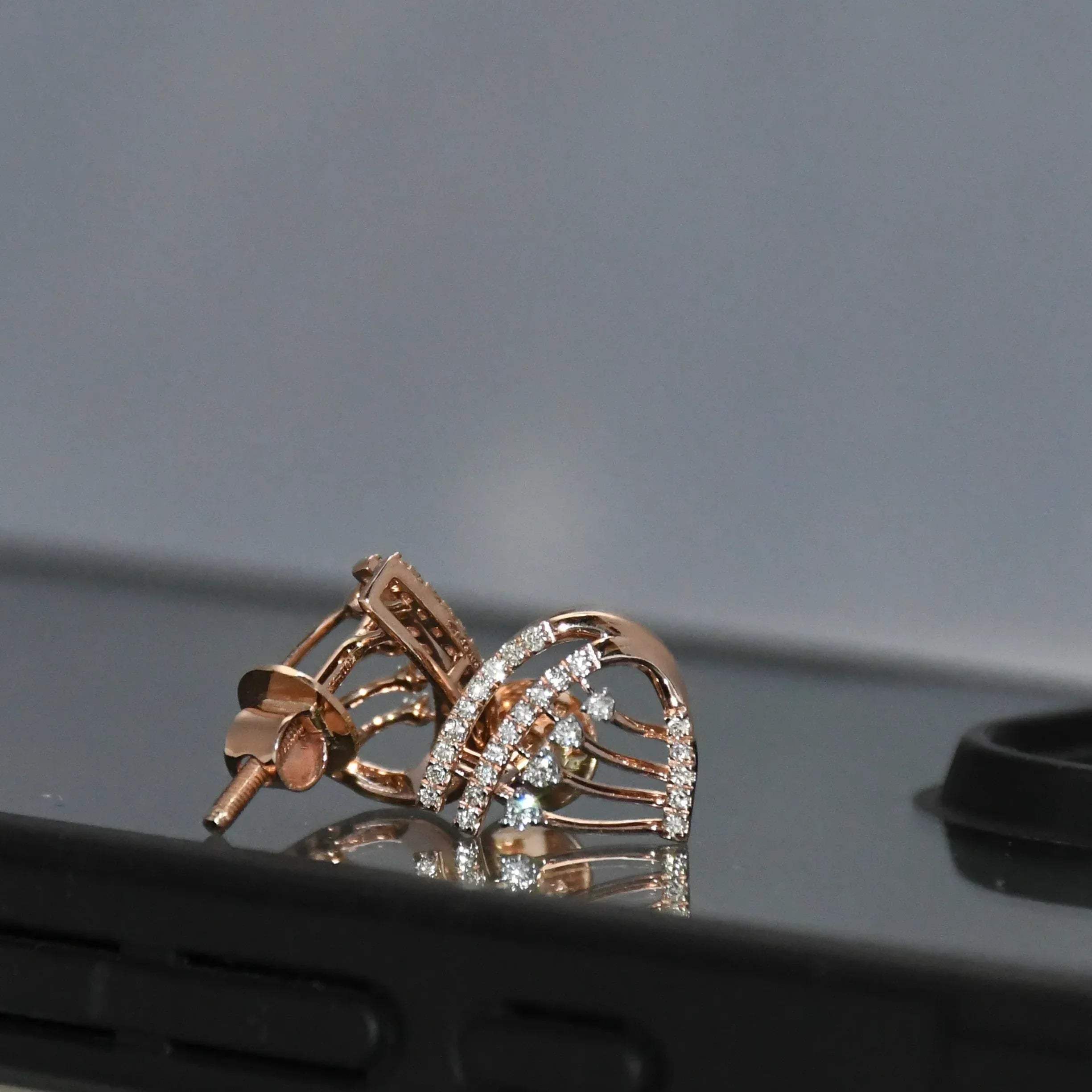 Rose gold earrings with diamonds on a reflective surface