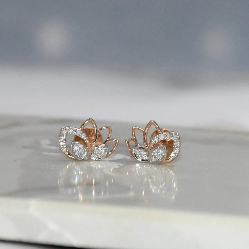 Rose gold lotus flower earrings with clear diamonds on a reflective surface.