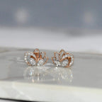 Rose gold lotus flower earrings with clear diamonds on a reflective surface.
