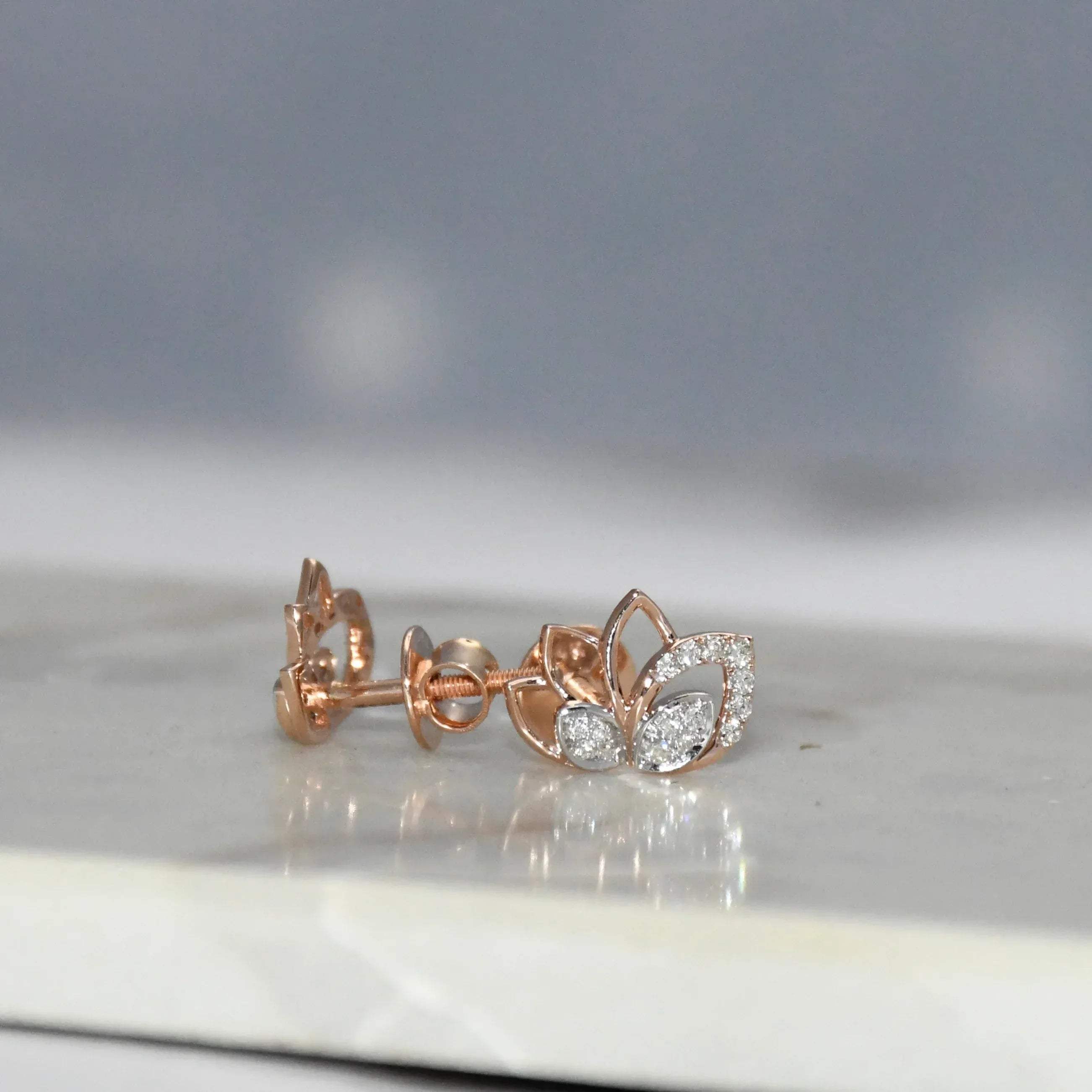 Rose gold earrings with diamond accents on a reflective surface