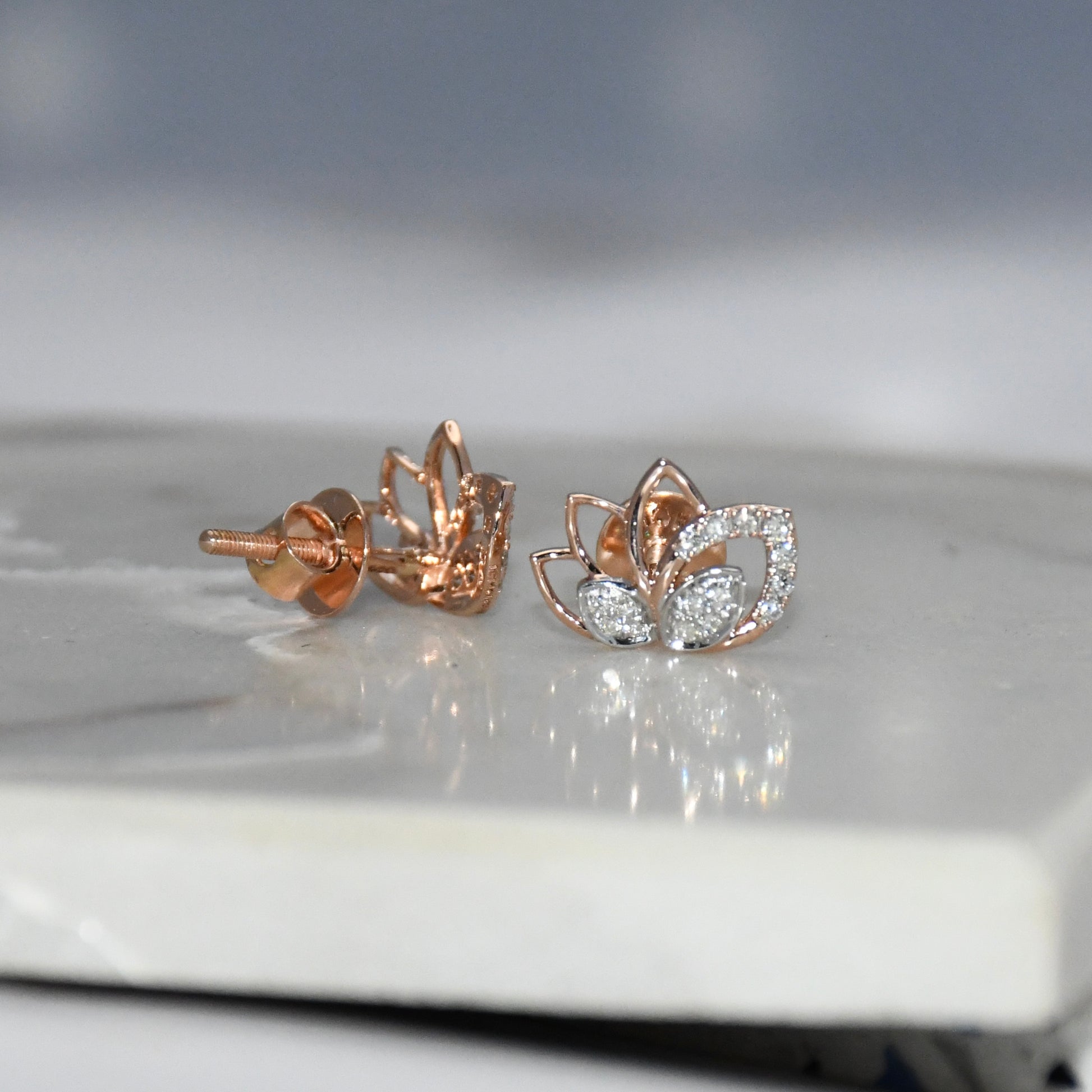 Rose gold lotus flower diamond earrings on a reflective surface
