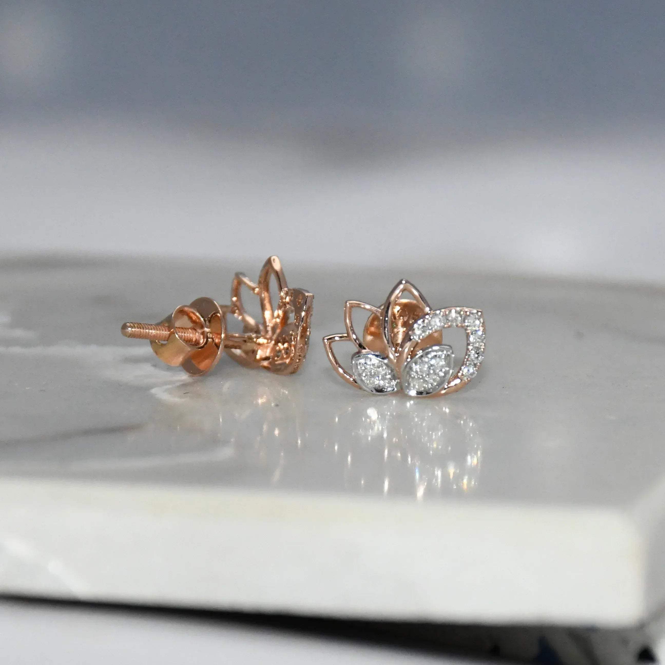 Rose gold lotus flower diamond earrings on a reflective surface