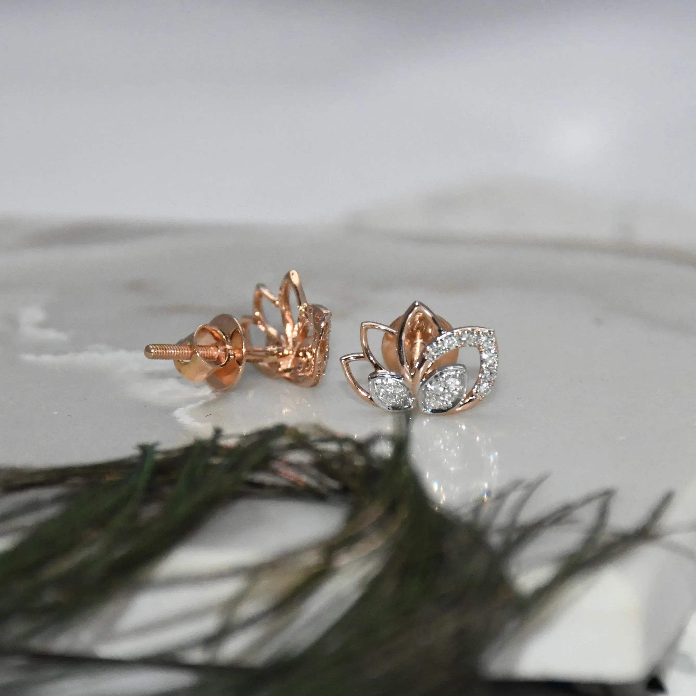 Rose gold lotus flower earrings with clear diamonds on a white surface.