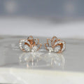 Rose gold lotus flower earrings with clear diamonds on a reflective surface.