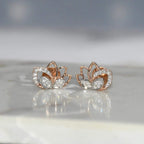 Rose gold lotus flower earrings with clear diamonds on a reflective surface.