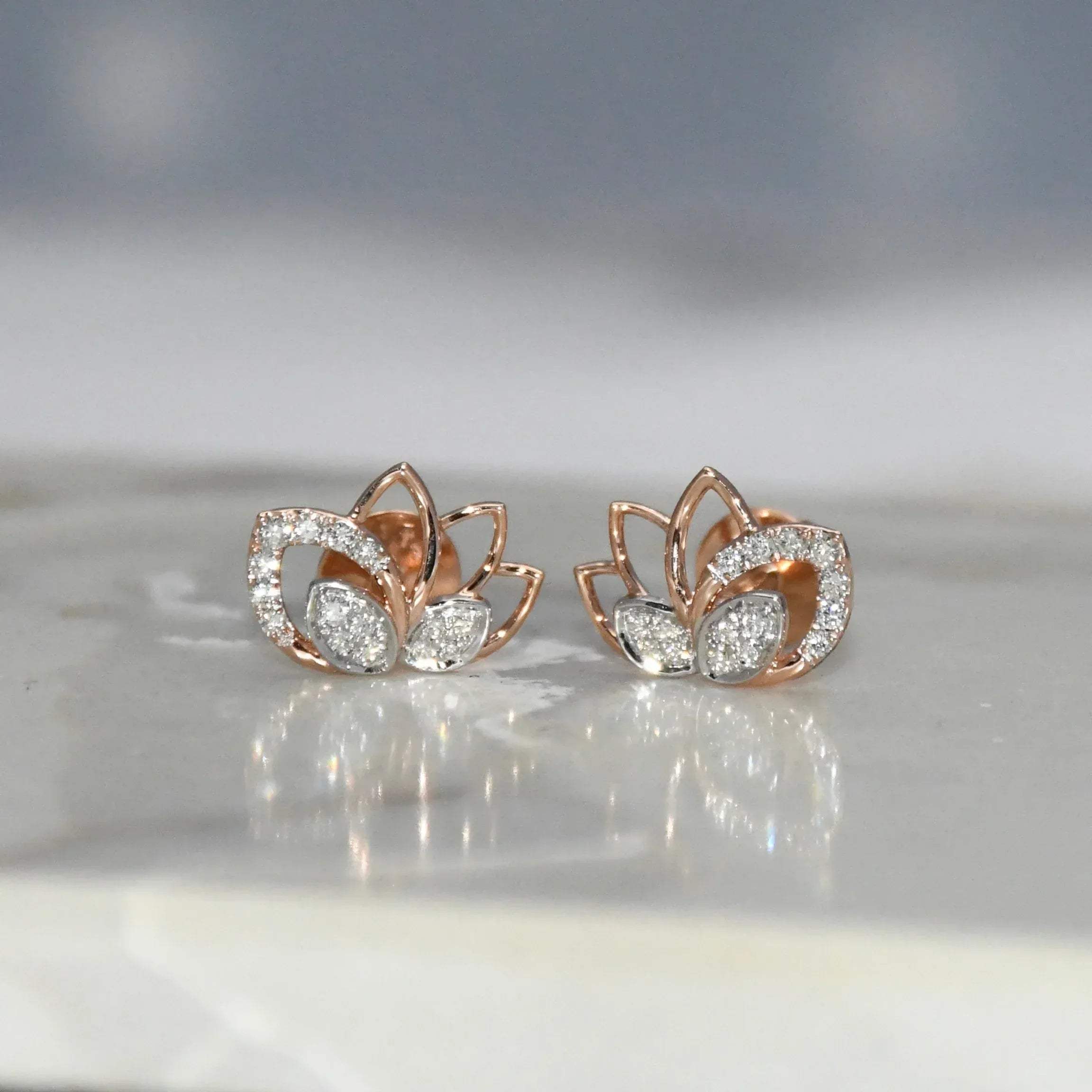 Rose gold lotus flower earrings with clear diamonds on a reflective surface.