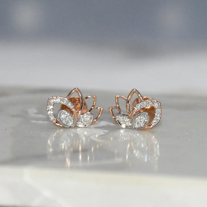 Rose gold lotus flower earrings with clear diamonds on a reflective surface.