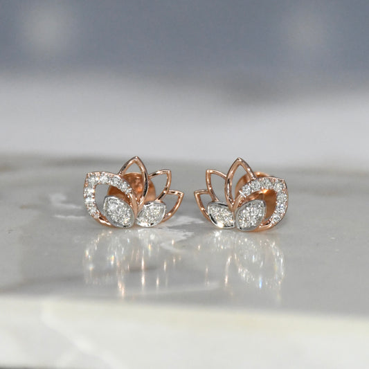 Rose gold lotus flower earrings with clear diamonds on a reflective surface.