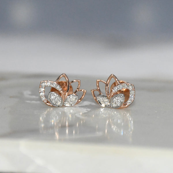 Rose gold lotus flower earrings with clear diamonds on a reflective surface.
