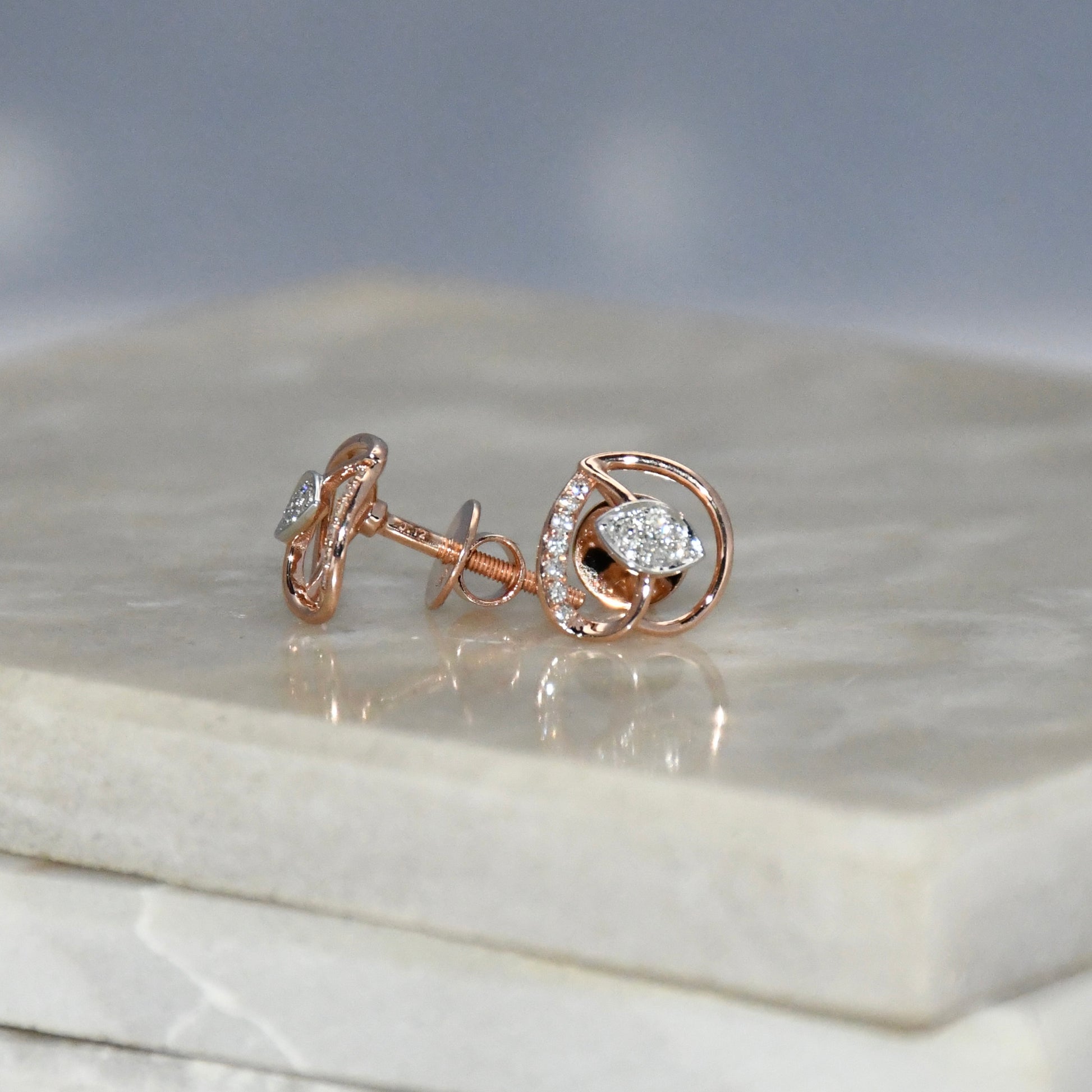 Rose gold earrings with diamond accents on a marble surface