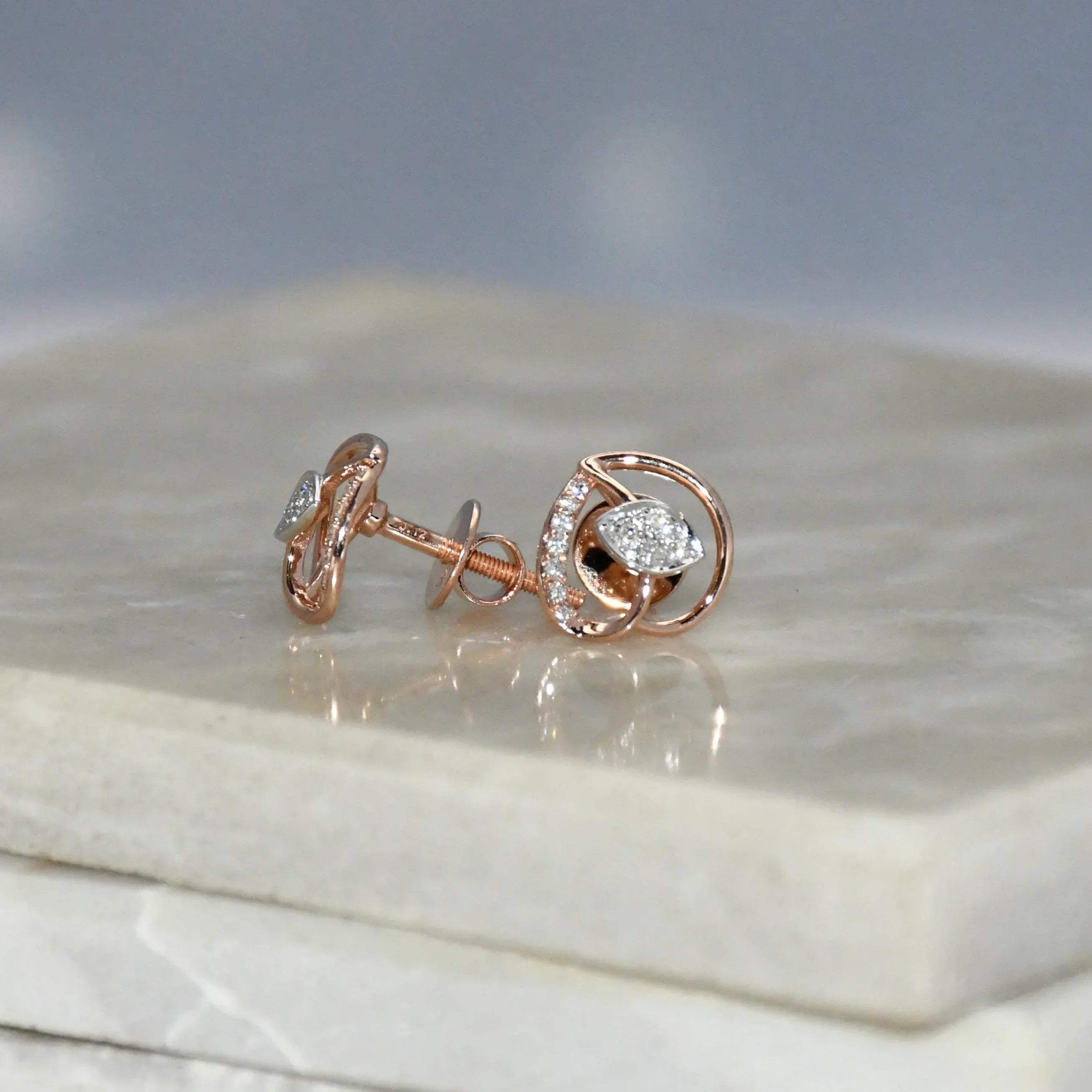 Rose gold earrings with diamond accents on a marble surface