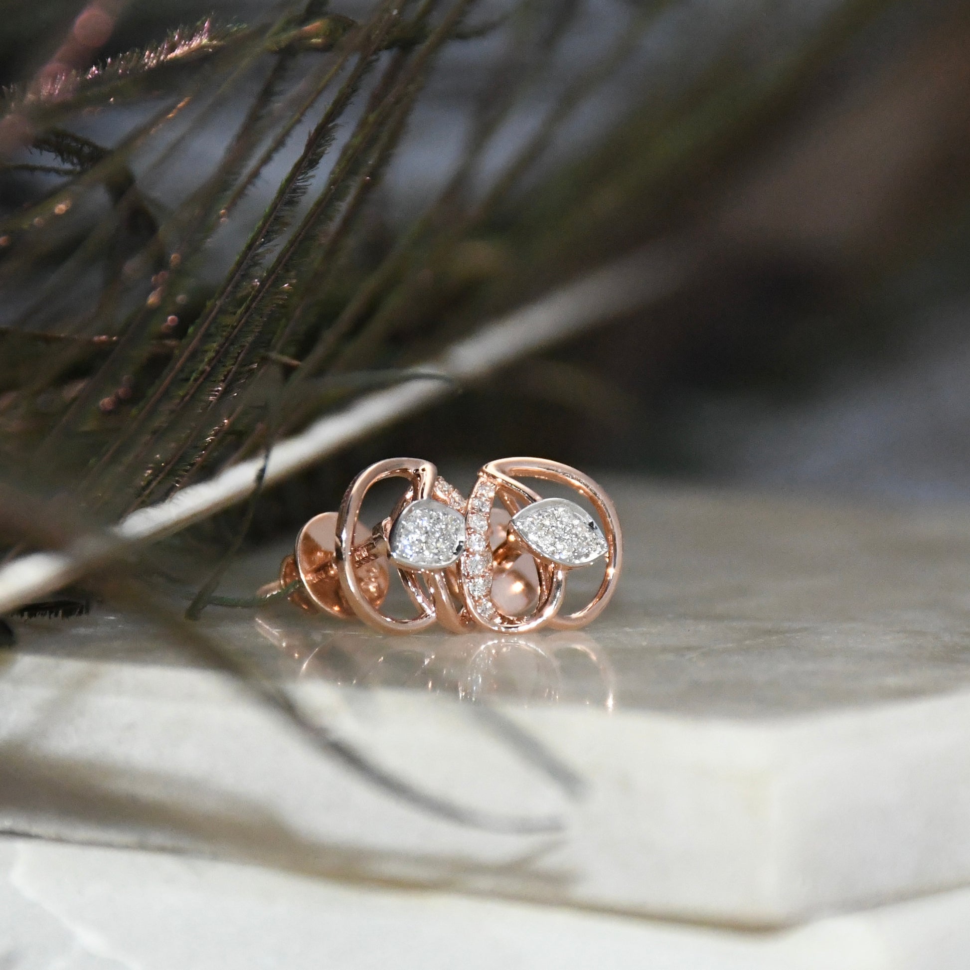 Rose gold earrings with diamonds accents on a textured surface