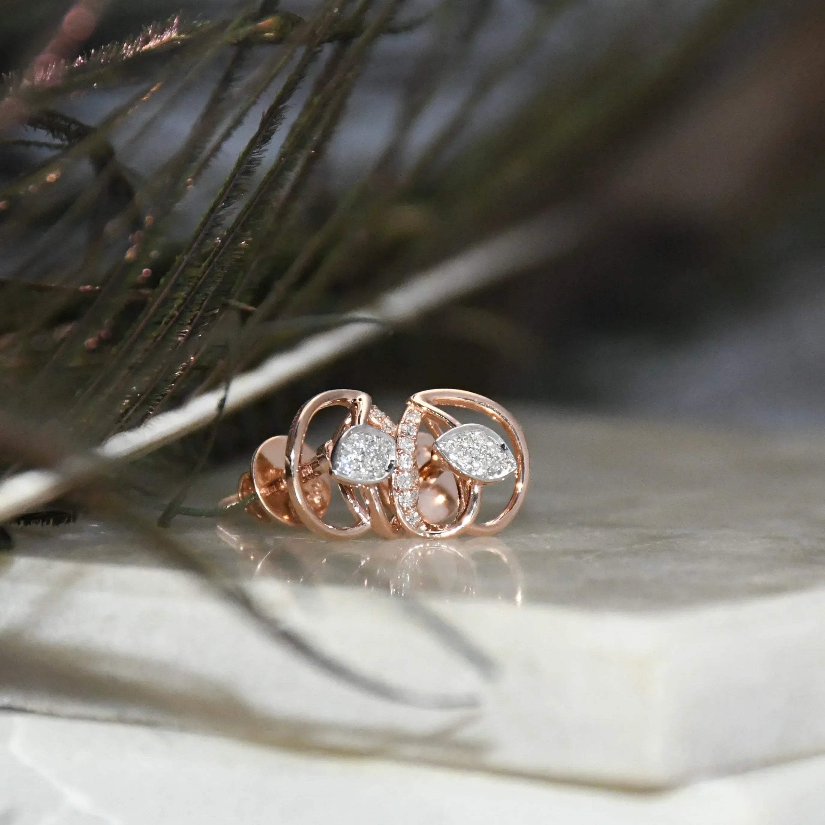 Rose gold earrings with diamonds accents on a textured surface