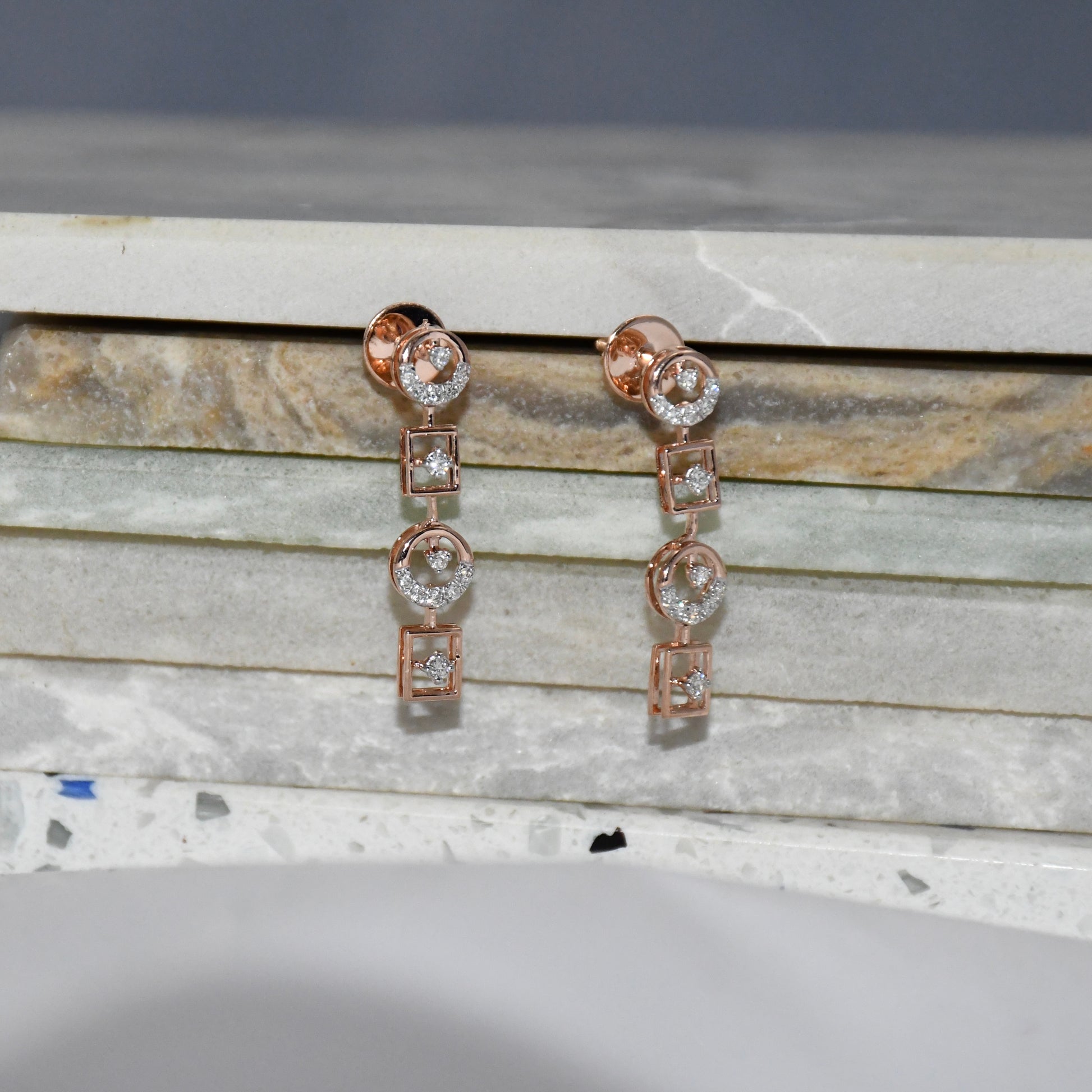 Rose gold earrings with diamonds on a marble surface
