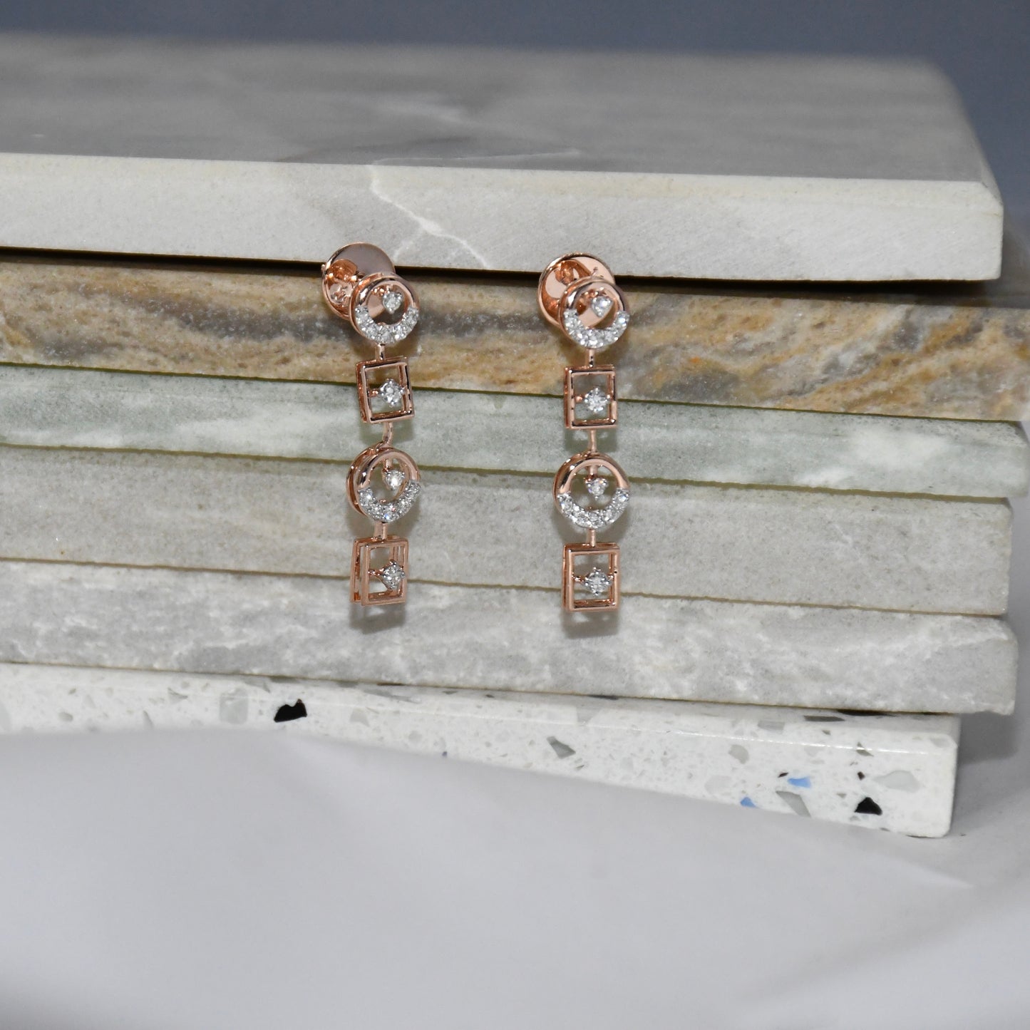 Rose gold earrings with clear diamonds on a marble surface