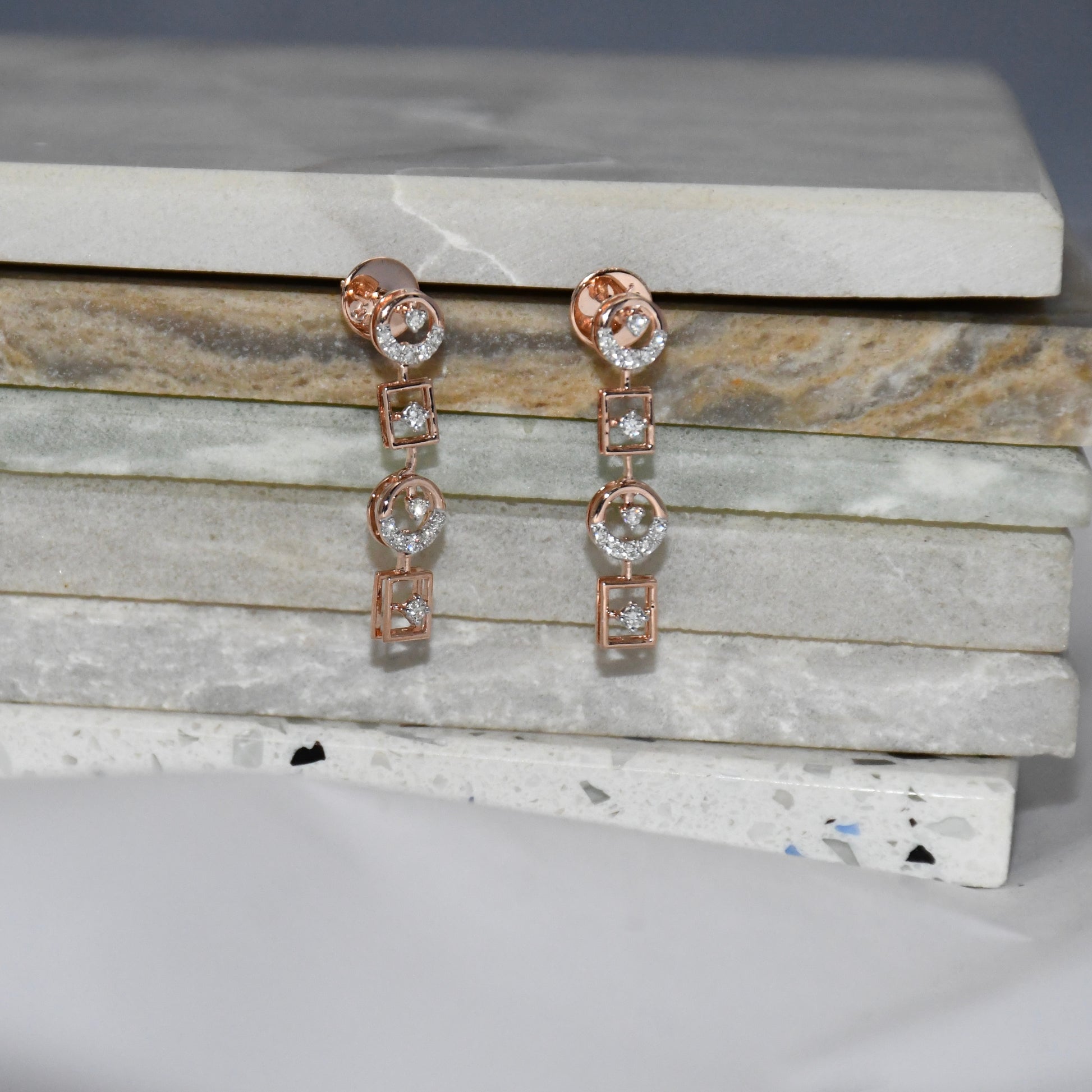 Rose gold earrings with clear diamonds on a marble surface