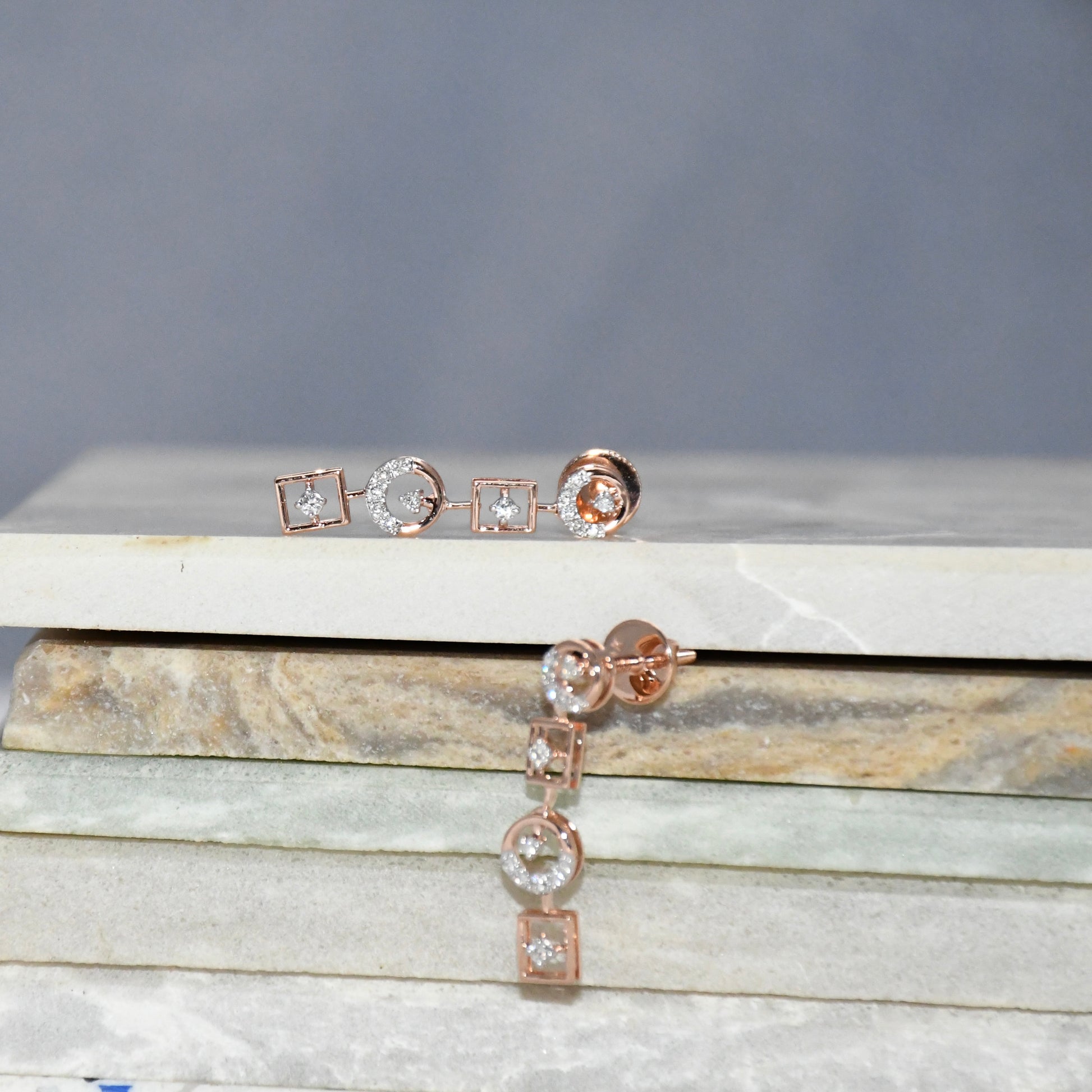 Rose gold earrings on a marble surface with a gray background