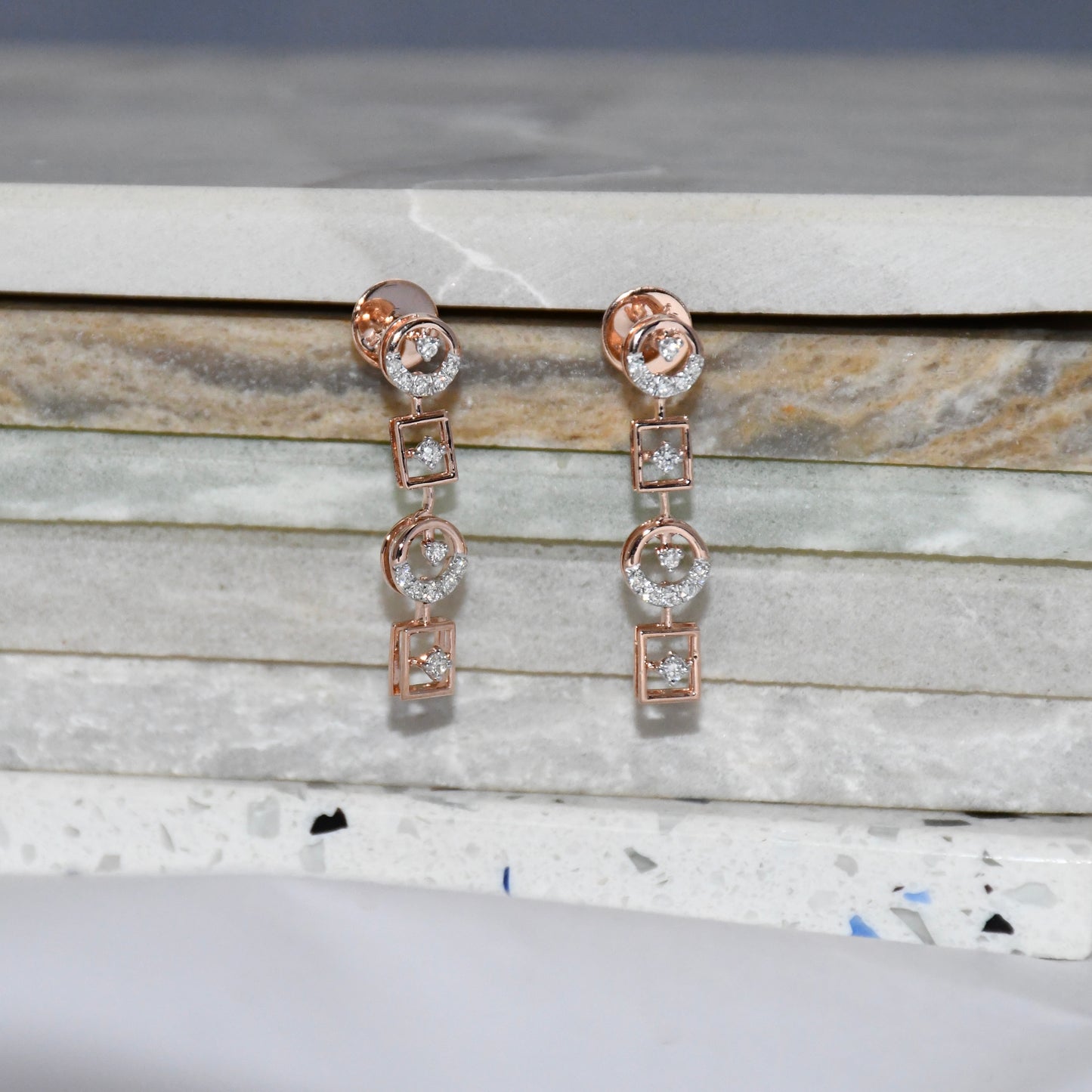 Rose gold earrings with diamonds on a marble surface
