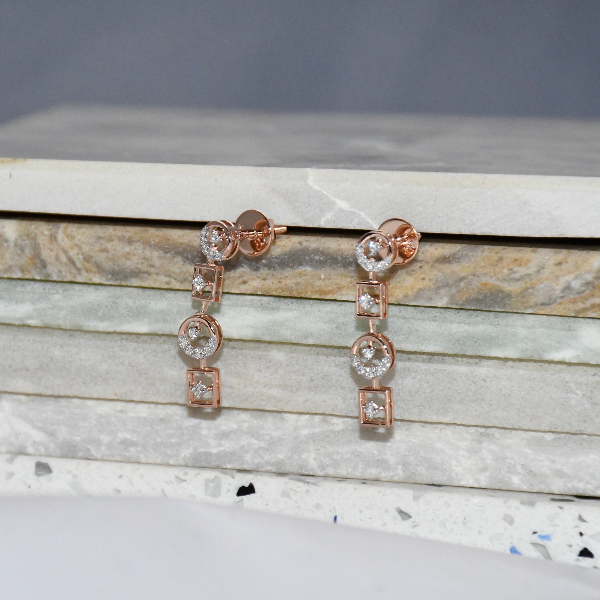 Rose gold earrings with clear diamonds on a marble surface