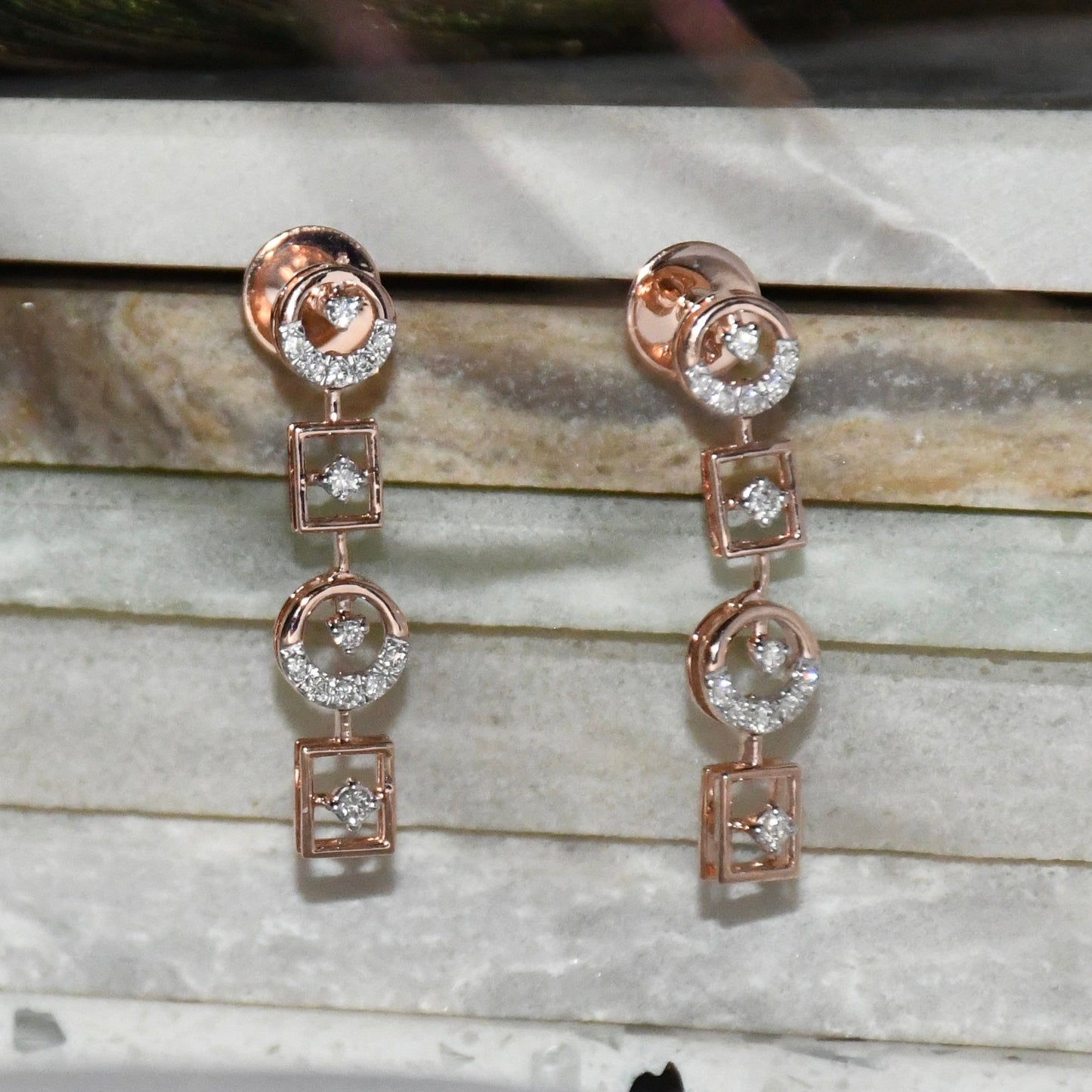Rose gold earrings with clear diamonds on a marble surface