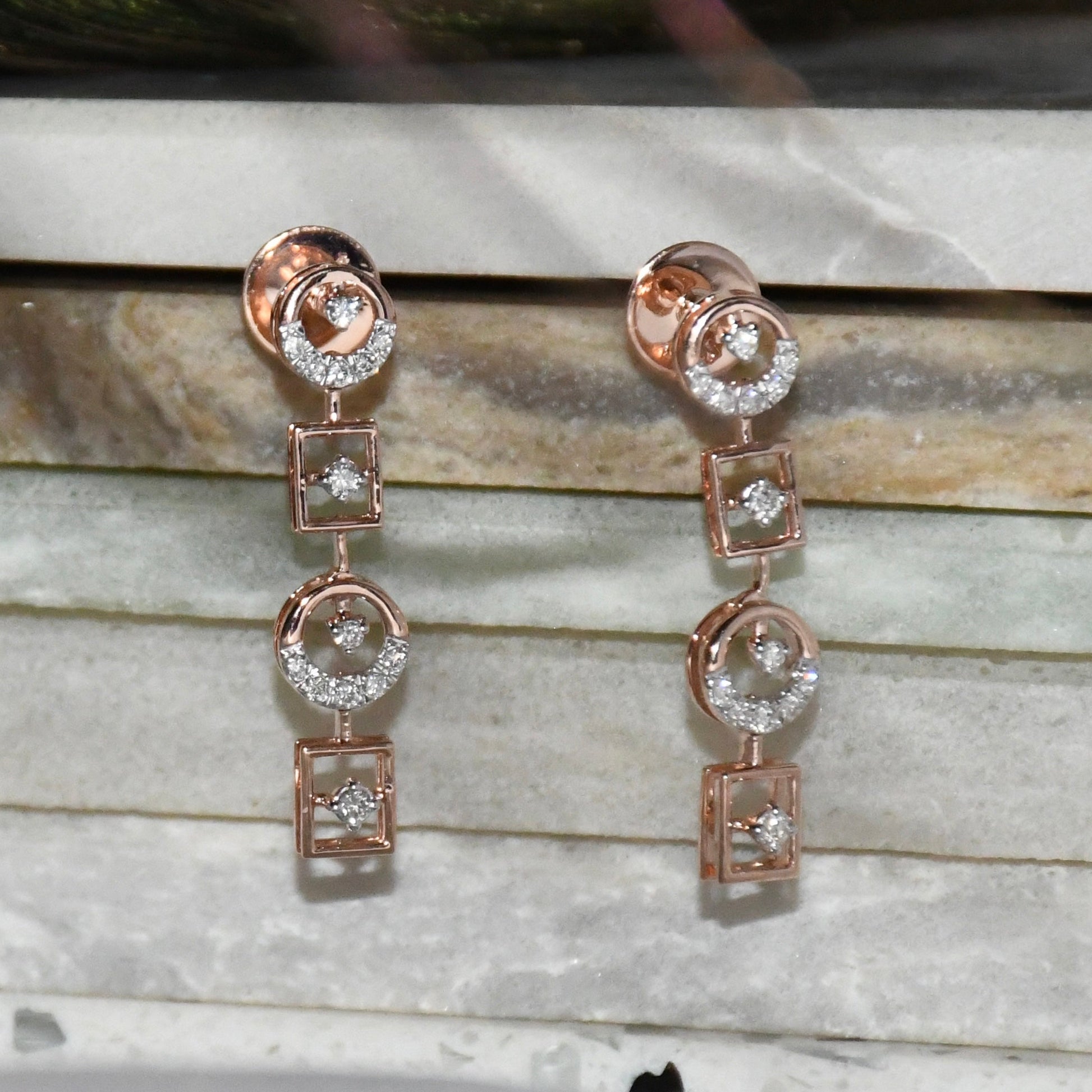 Rose gold earrings with clear diamonds on a marble surface