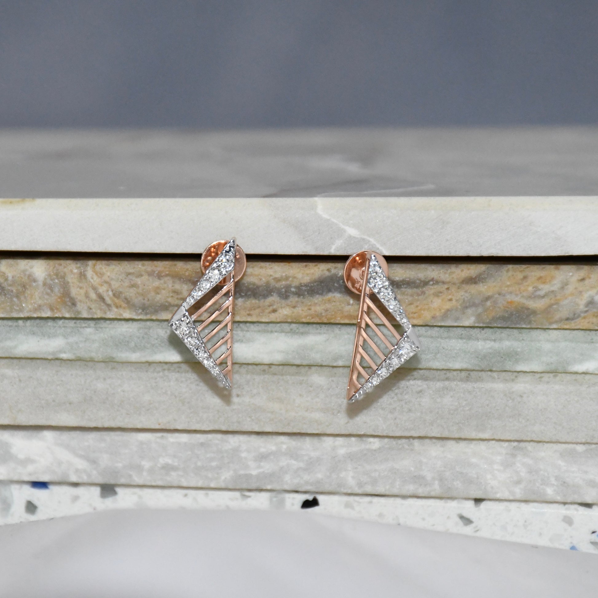 Pair of gold and diamond geometric earrings on a marble surface.