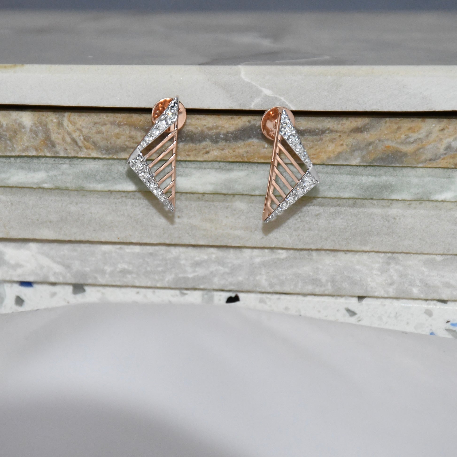 Pair of gold and diamond geometric earrings on a marble surface.