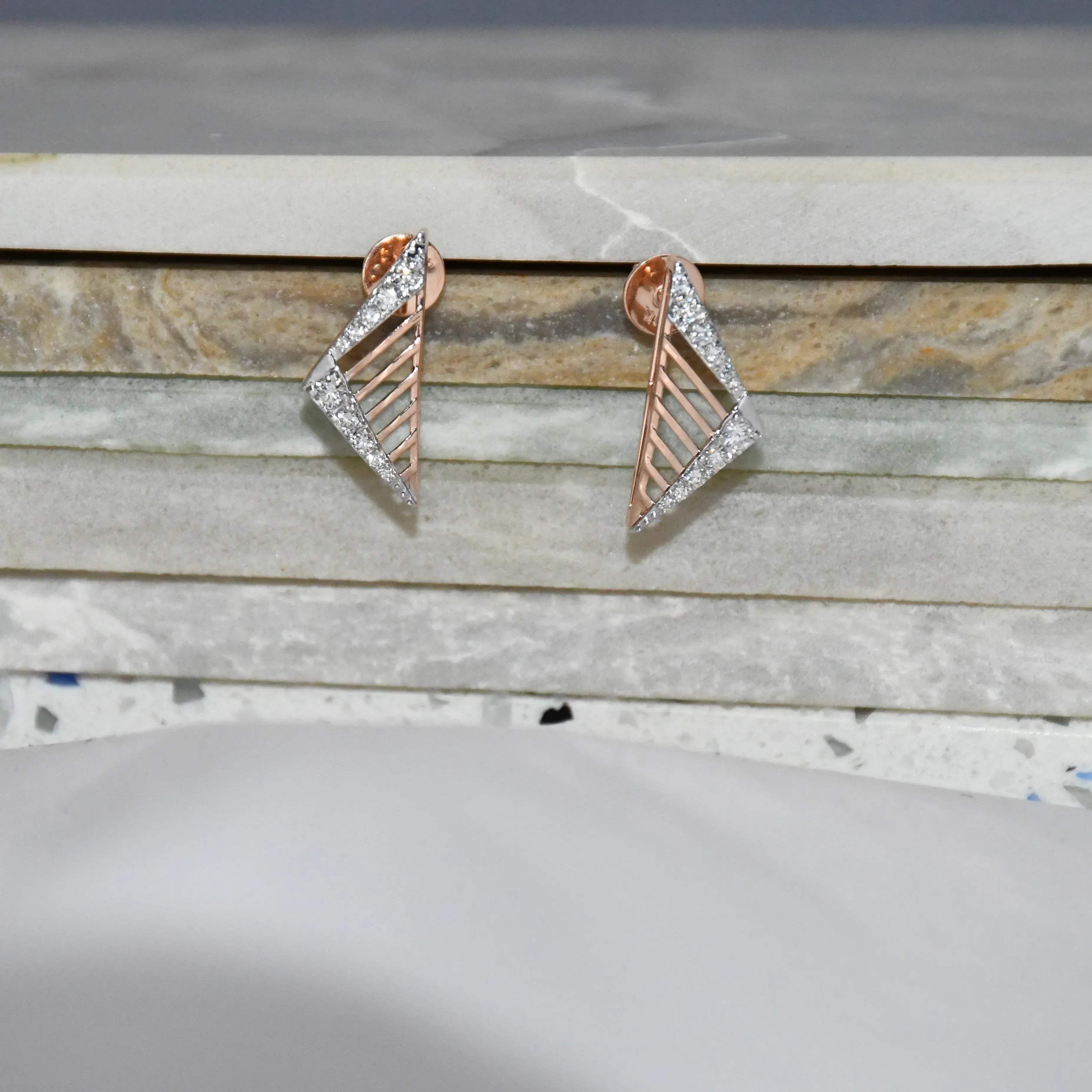 Pair of gold and diamond geometric earrings on a marble surface.