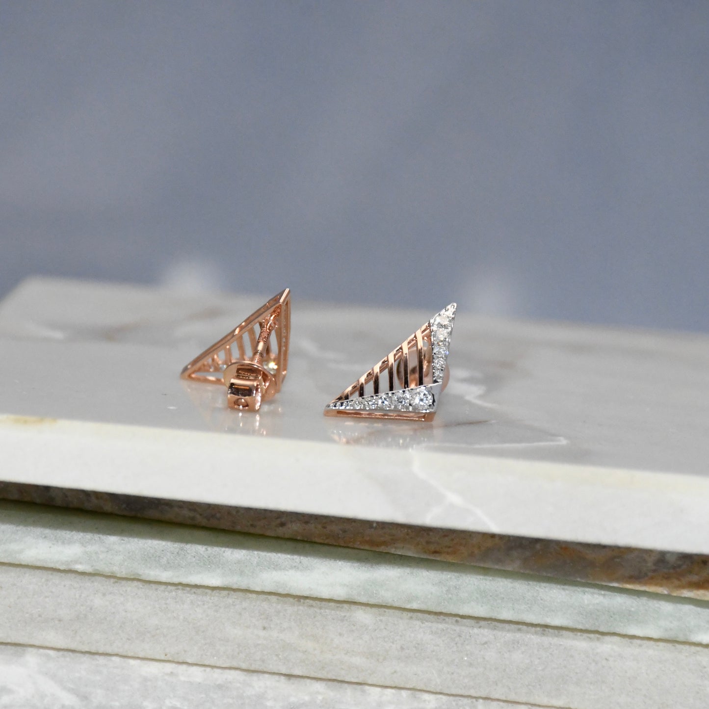 Gold triangle-shaped diamond earrings on a marble surface with a gray background