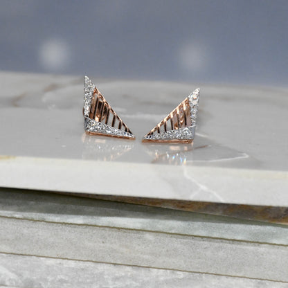 Gold triangle-shaped diamond earrings on a marble surface with a gray background.
