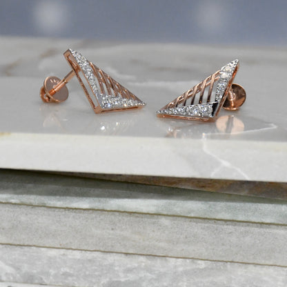Gold triangle-shaped diamond earrings on a marble surface with a gray background.