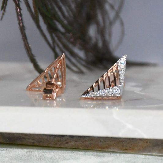 Gold and diamond earrings on a marble surface with a plant in the background.