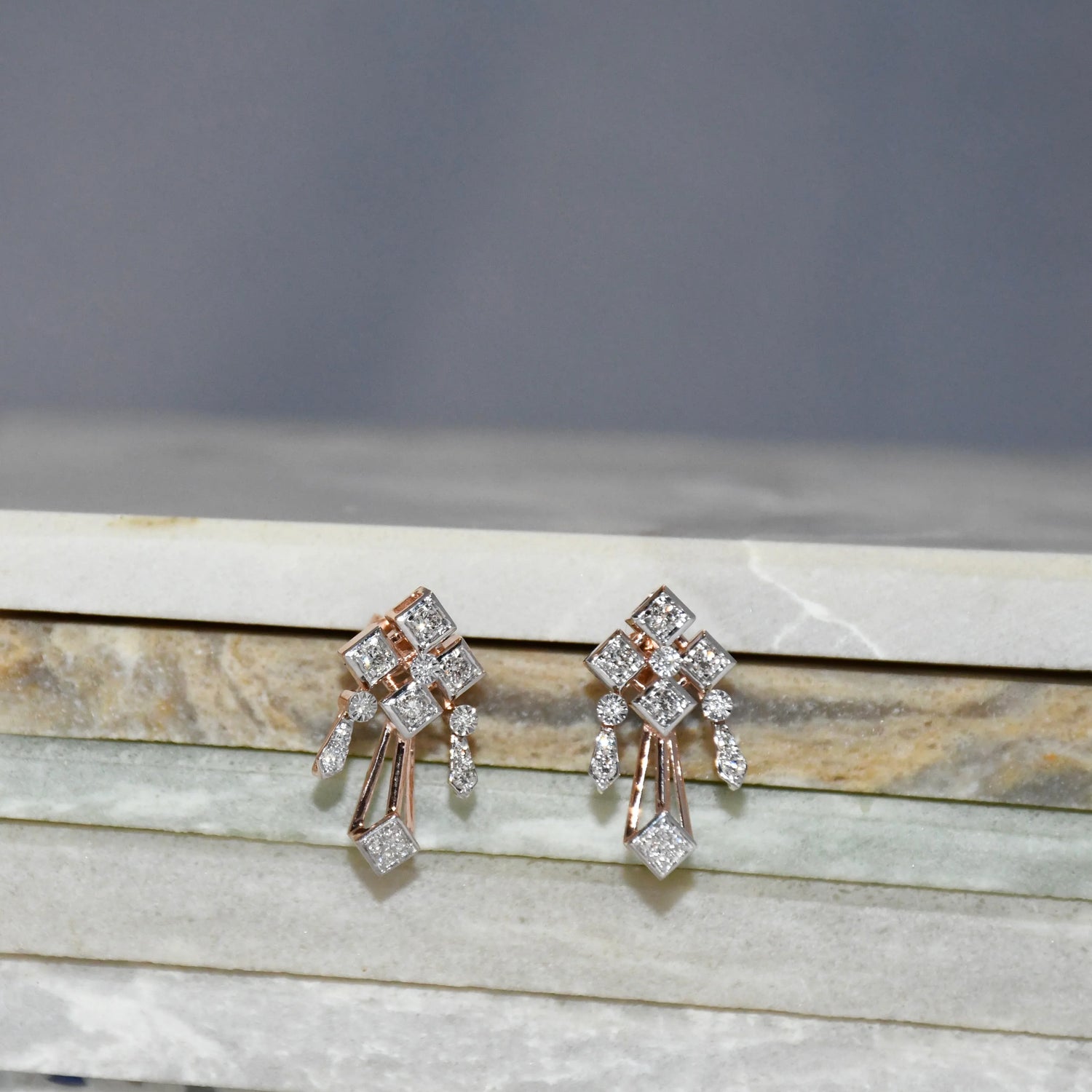 Pair of diamond earrings on a marble surface with a gray background