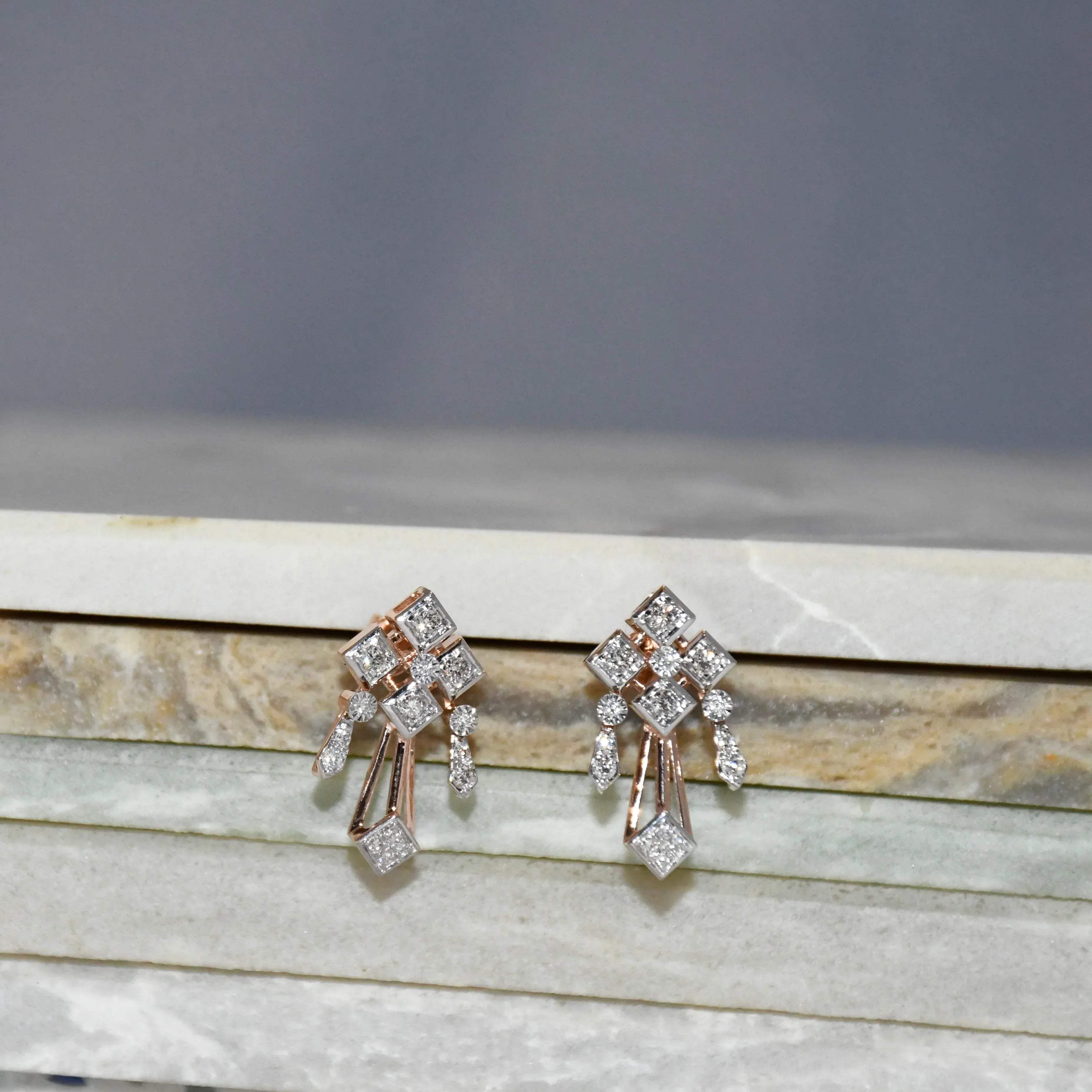 Pair of diamond earrings on a marble surface with a gray background