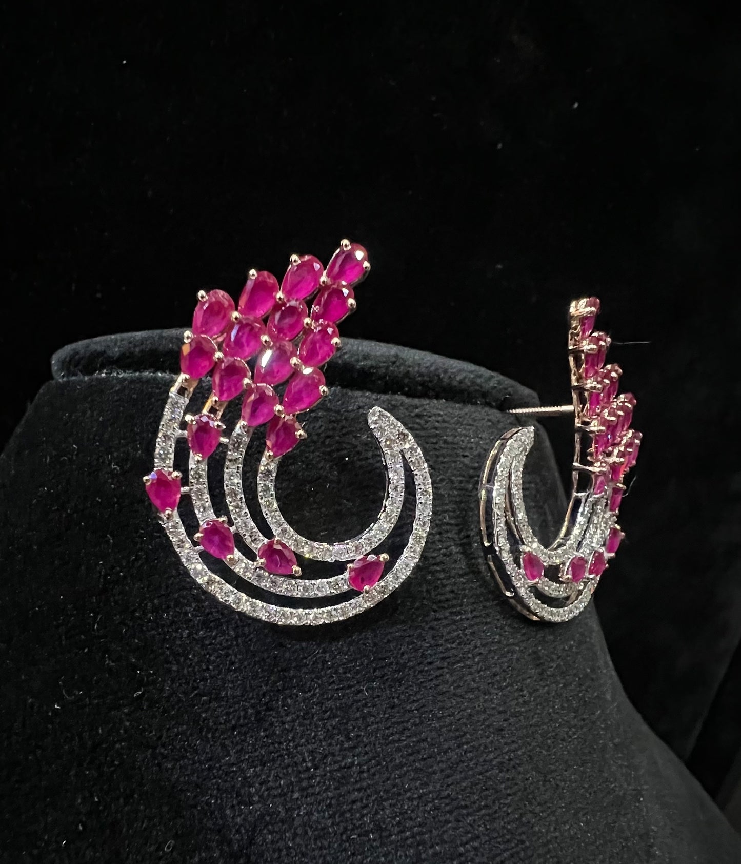 Pair of color stone and diamond swirl earrings with multiple pear-shaped color stones and round diamonds set in a circular design on a black display stand.