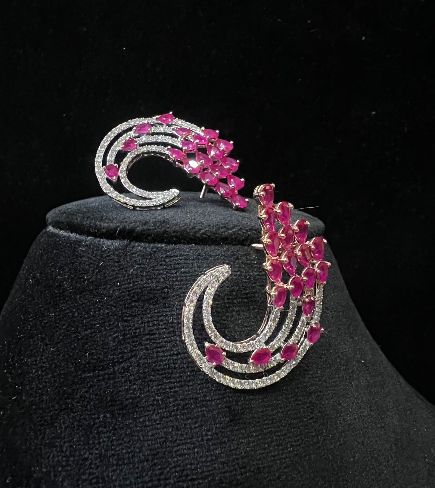 Pair of color stone and diamond swirl earrings with multiple pear-shaped color stones and round diamonds set in a circular design on a black display stand.