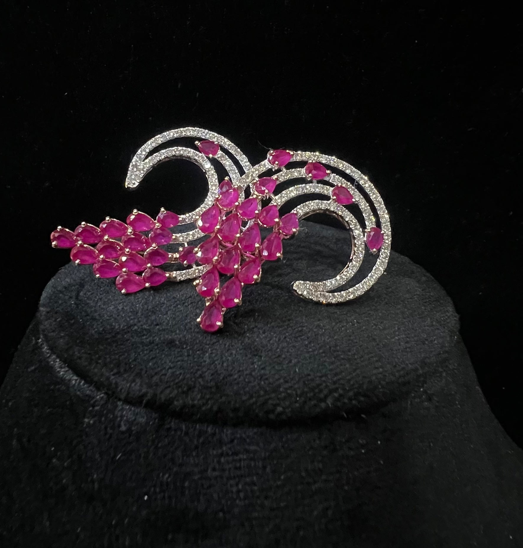 Pair of color stone and diamond swirl earrings with multiple pear-shaped color stones and round diamonds set in a circular design on a black display stand.