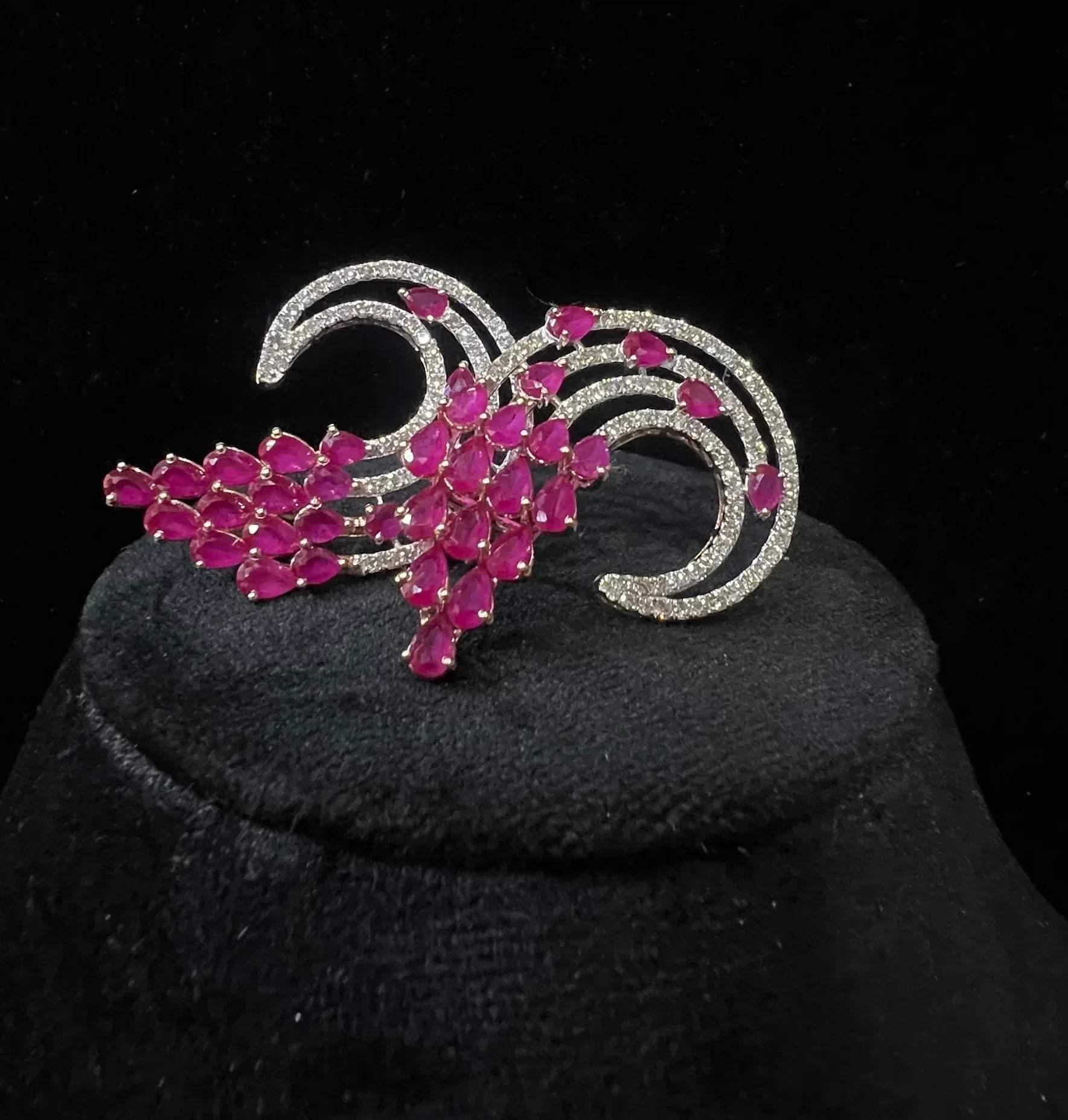 Pair of color stone and diamond swirl earrings with multiple pear-shaped color stones and round diamonds set in a circular design on a black display stand.