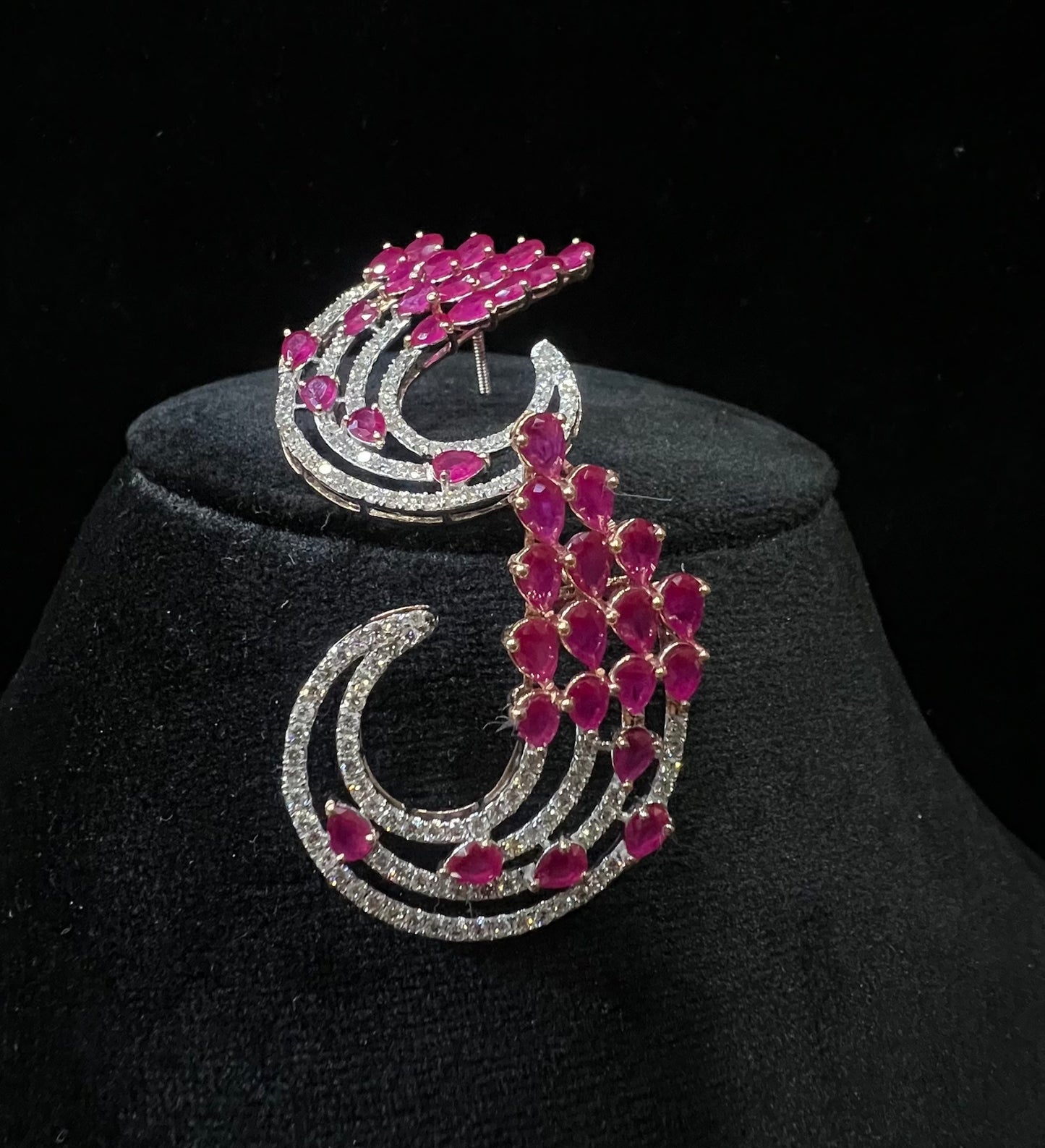 Pair of color stone and diamond swirl earrings with multiple pear-shaped color stones and round diamonds set in a circular design on a black display stand.