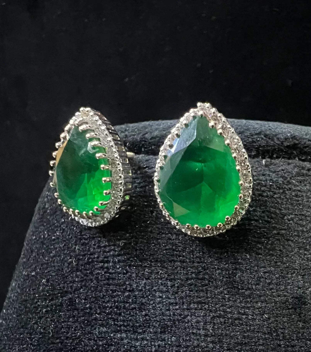 Pair of teardrop green stone and diamond halo earrings displayed on a black stand.