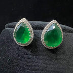 Pair of teardrop green stone and diamond halo earrings displayed on a black stand.